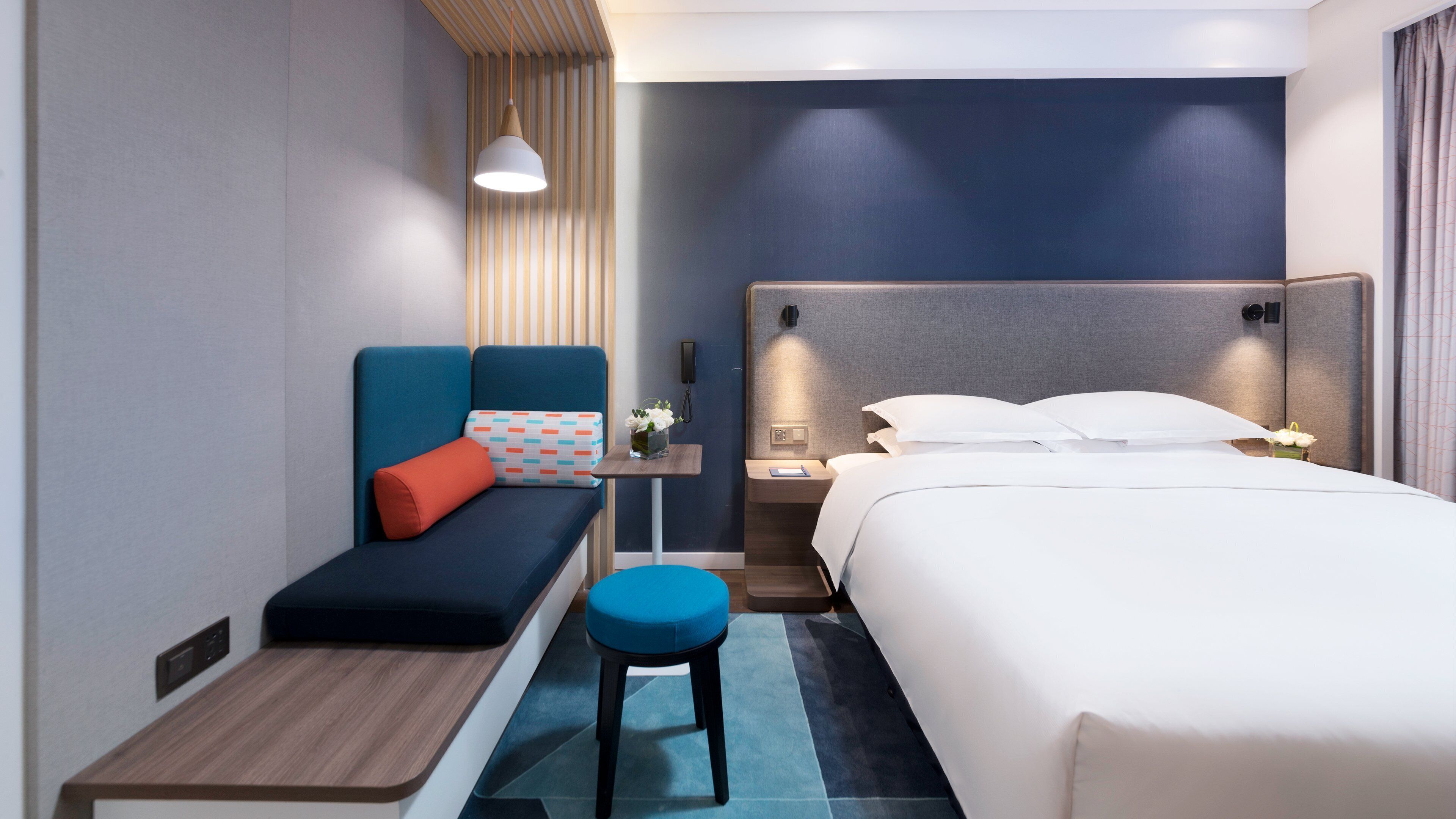 Een hotelkamer met een bed, een zithoek met een bank en een kleine tafel, een nachtkastje met een lamp en een aan de muur bevestigd telefoon.