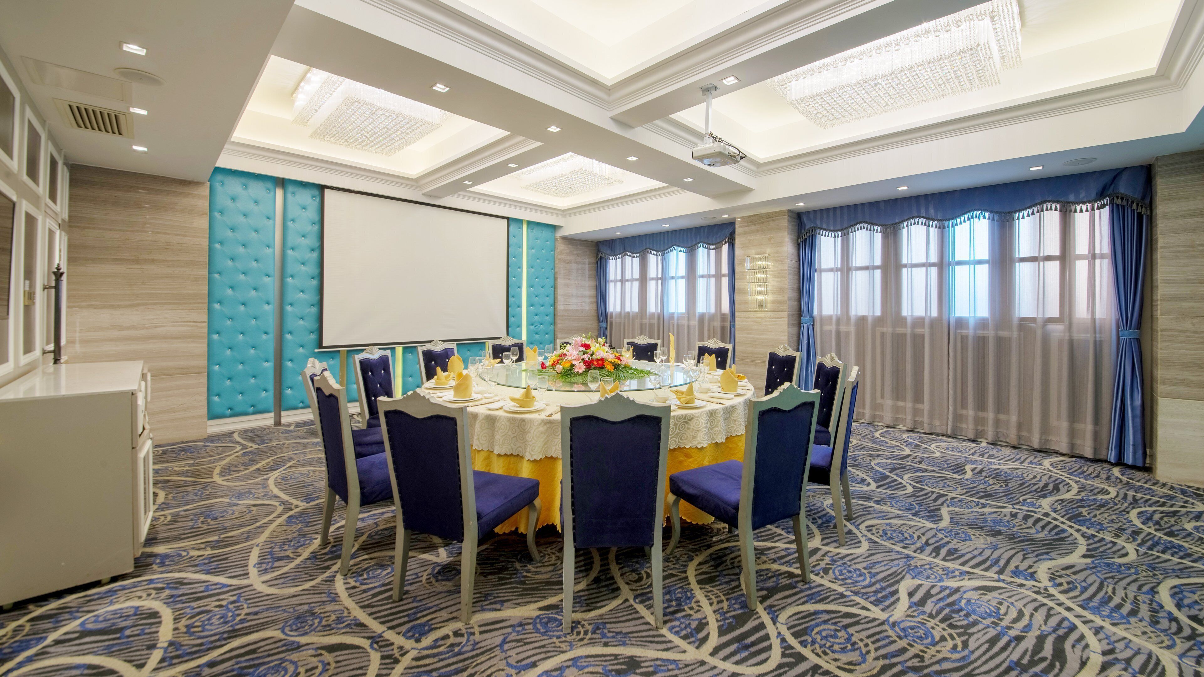 A conference room with a round table, chairs, a projector screen, and a carpeted floor.