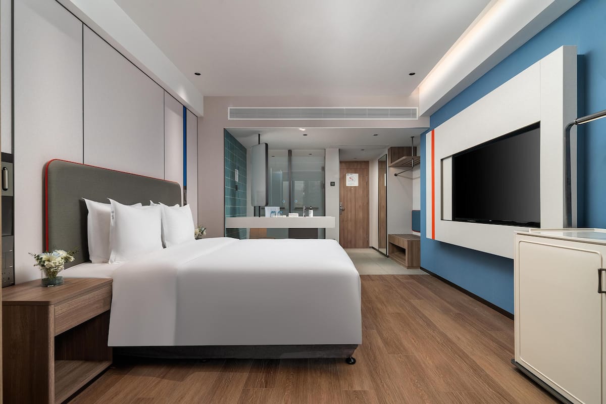 A modern hotel room with a large bed, a TV, a desk, and a wardrobe.