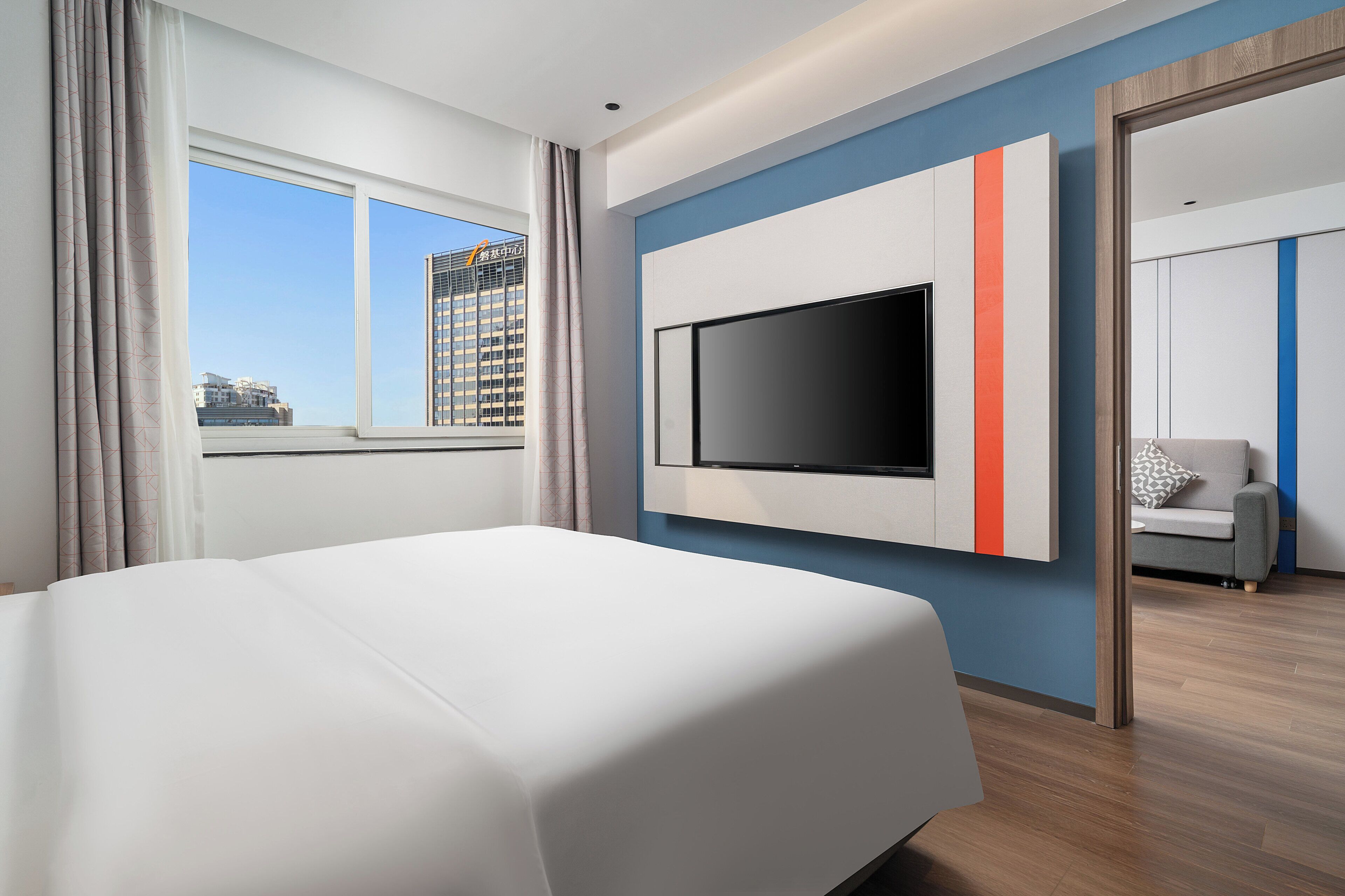 Une chambre d’hôtel avec un lit, une télévision, une vue sur la ville et une porte donnant sur une autre pièce.