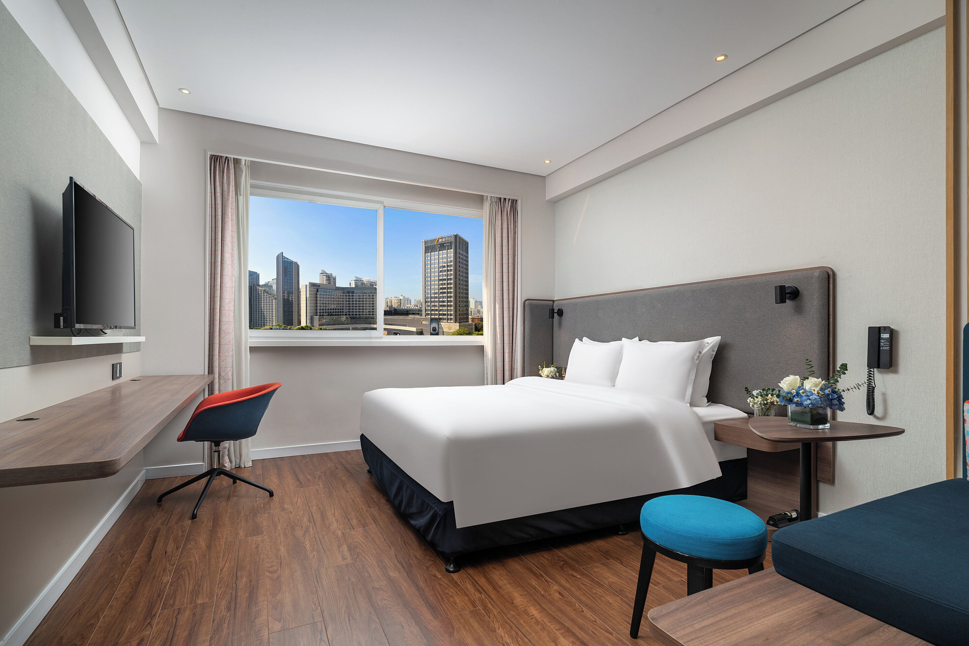 Une chambre d’hôtel moderne dotée d’un grand lit, d’un bureau, d’une chaise, d’une télévision et offrant une vue sur le paysage urbain.