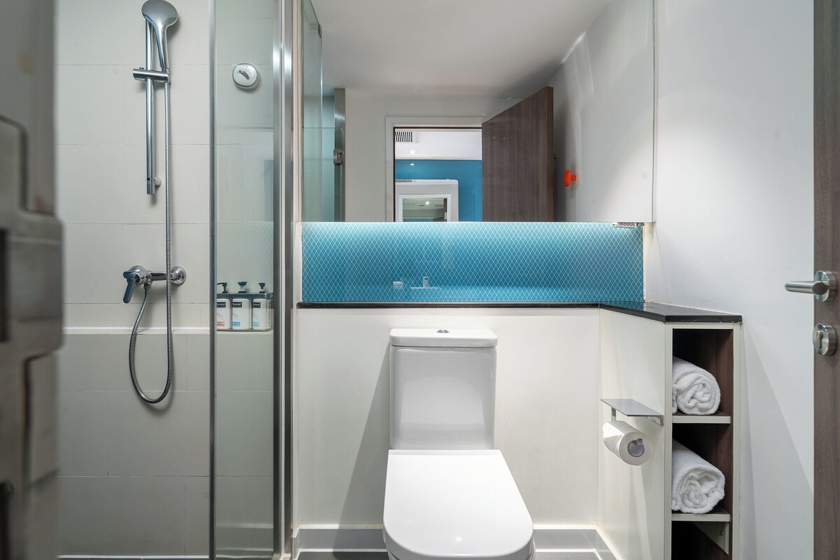 A modern bathroom with a glass shower enclosure, a white toilet, and a blue-tiled sink area.