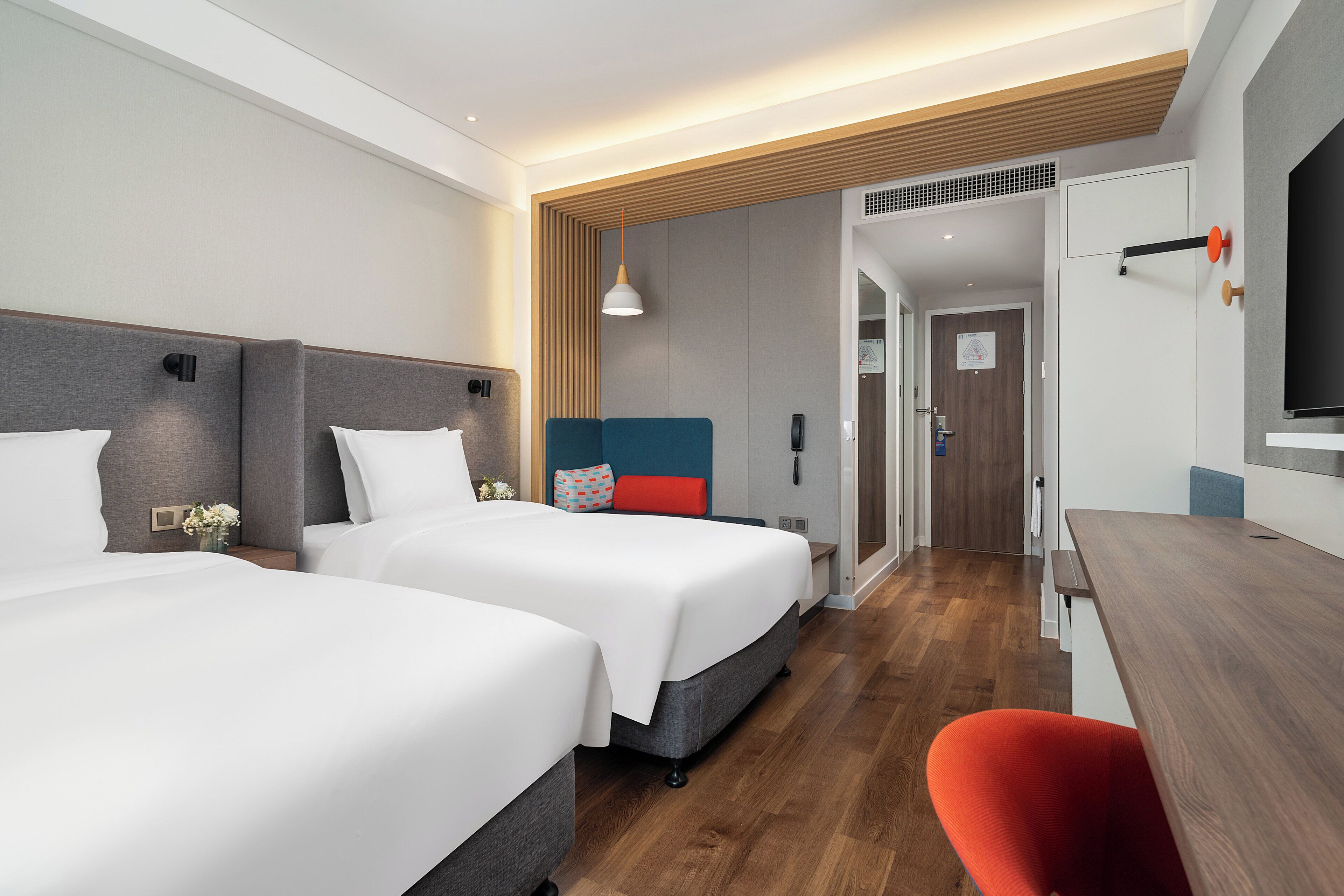 A hotel room with two beds, a desk, a chair, a TV, and a shower area.