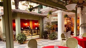 A café with round tables and chairs, a counter with a display case, and potted plants. - The Elgin Fairlawn Kolkata (Kolkata)