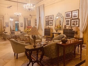 Un salon spacieux agrémenté d’un lustre, de fauteuils, d’un canapé et d’une cheminée.