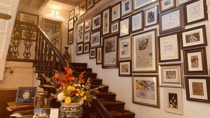 A staircase with framed photographs and certificates on the wall, a vase with flowers, and a table with a book and a framed certificate. - The Elgin Fairlawn Kolkata (Kolkata)