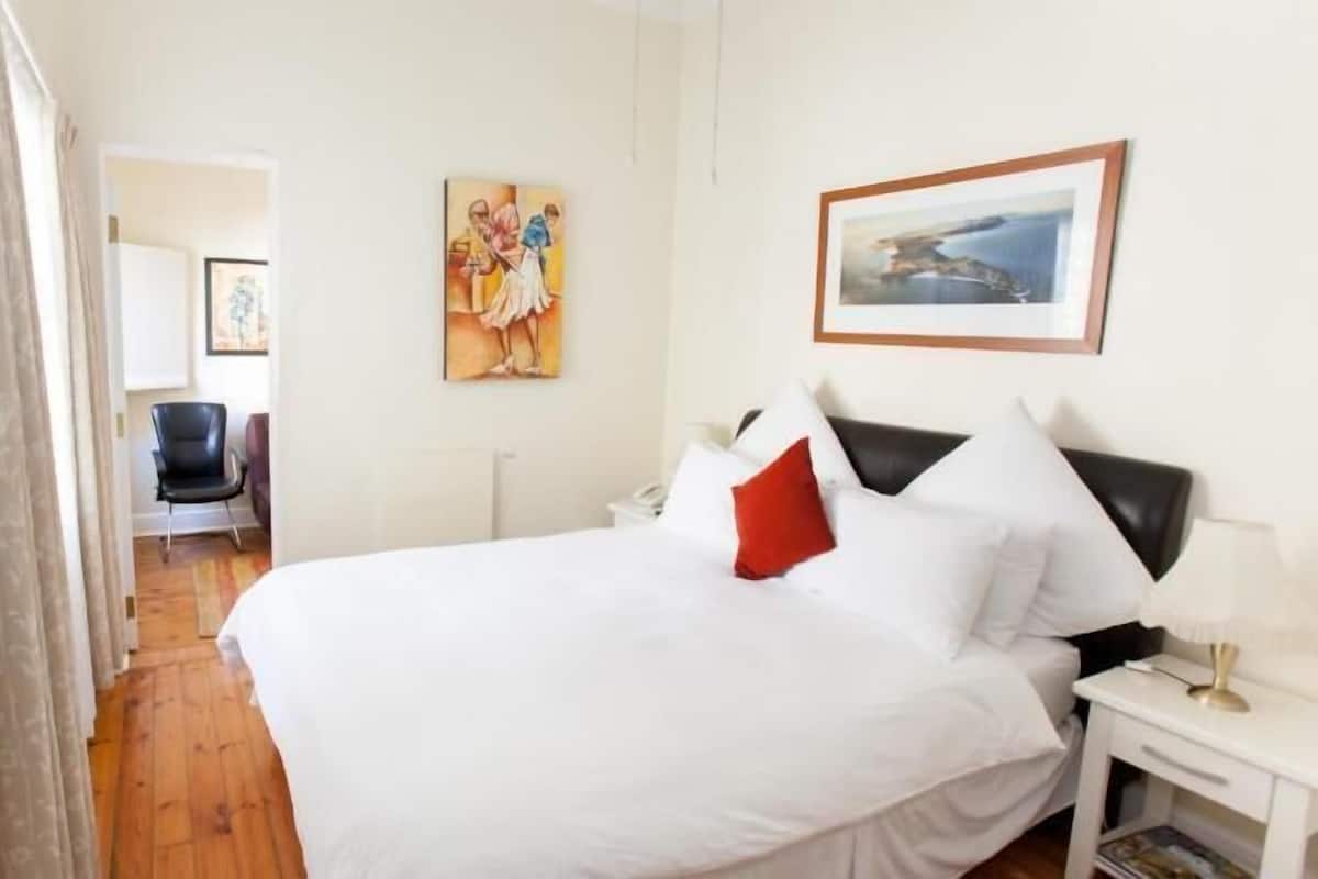 Habitació d'hotel amb un llit, una tauleta de nit, una cadira i obres d'art a les parets.