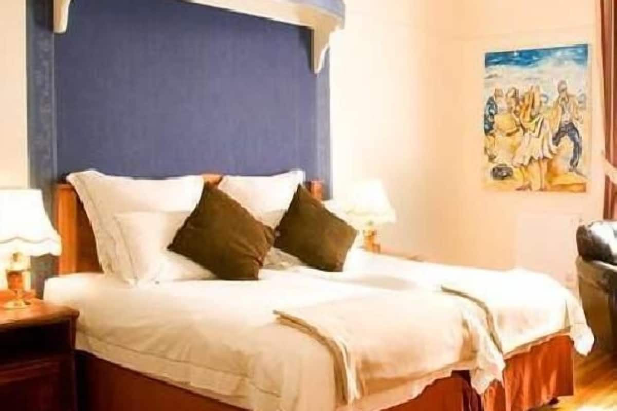 Habitació d'hotel amb un llit, una tauleta de nit, un quadre a la paret i una finestra.
