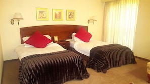 Habitación de hotel con dos camas, cada una con almohada roja y colcha negra. Encima de las camas hay tres cuadros enmarcados en la pared.