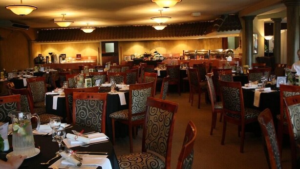 A restaurant with multiple tables and chairs, a kitchen area in the background, and hanging light fixtures. - Benvenuto Conference and Train (Randburg)