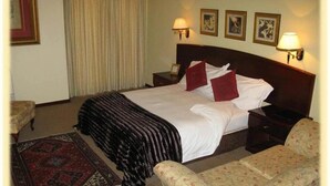 A hotel room with a large bed, two bedside tables with lamps, a red and black patterned rug, and two armchairs. - Benvenuto Conference and Train (Randburg)