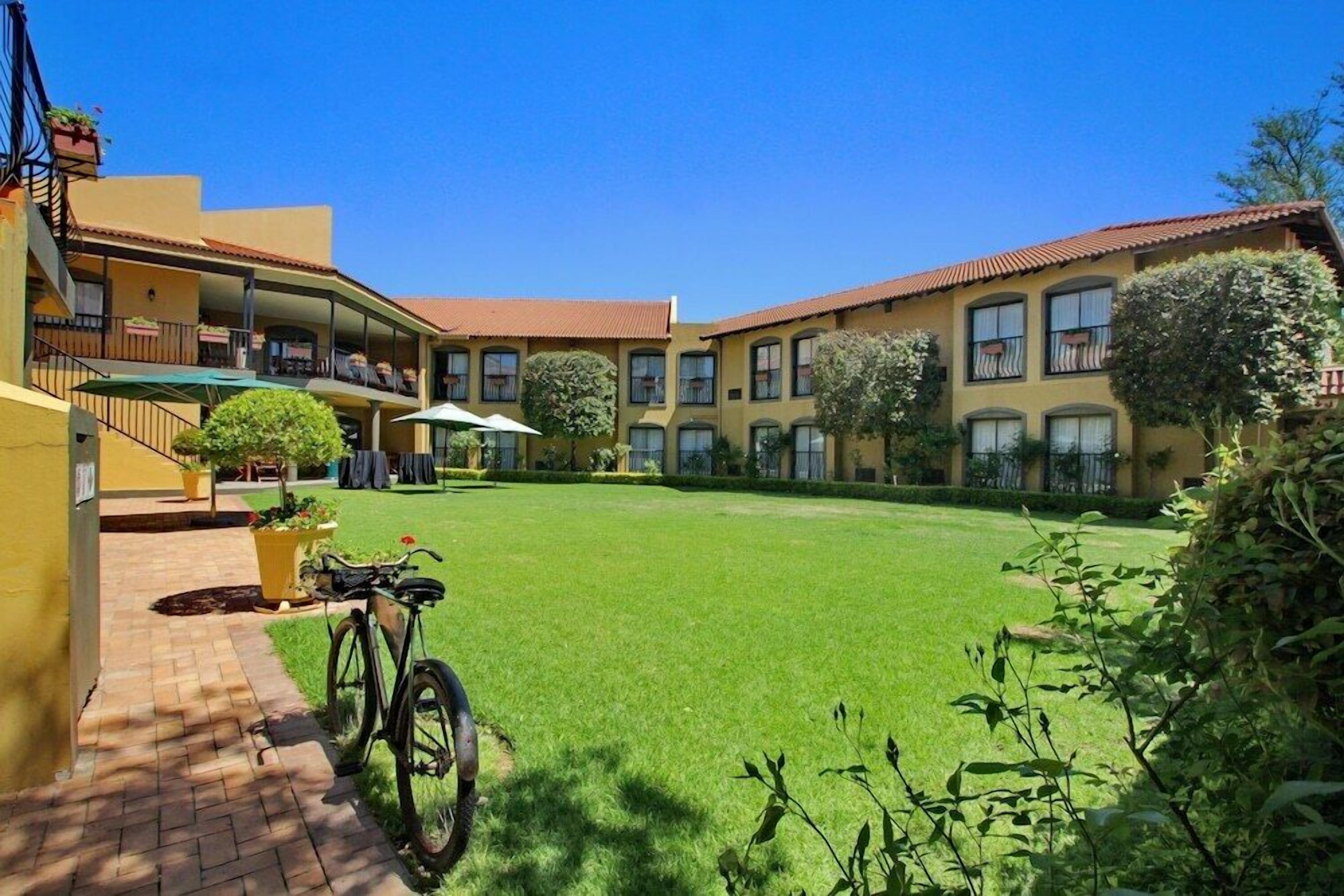 A courtyard with a green lawn, a bicycle, and a building with multiple balconies and windows.