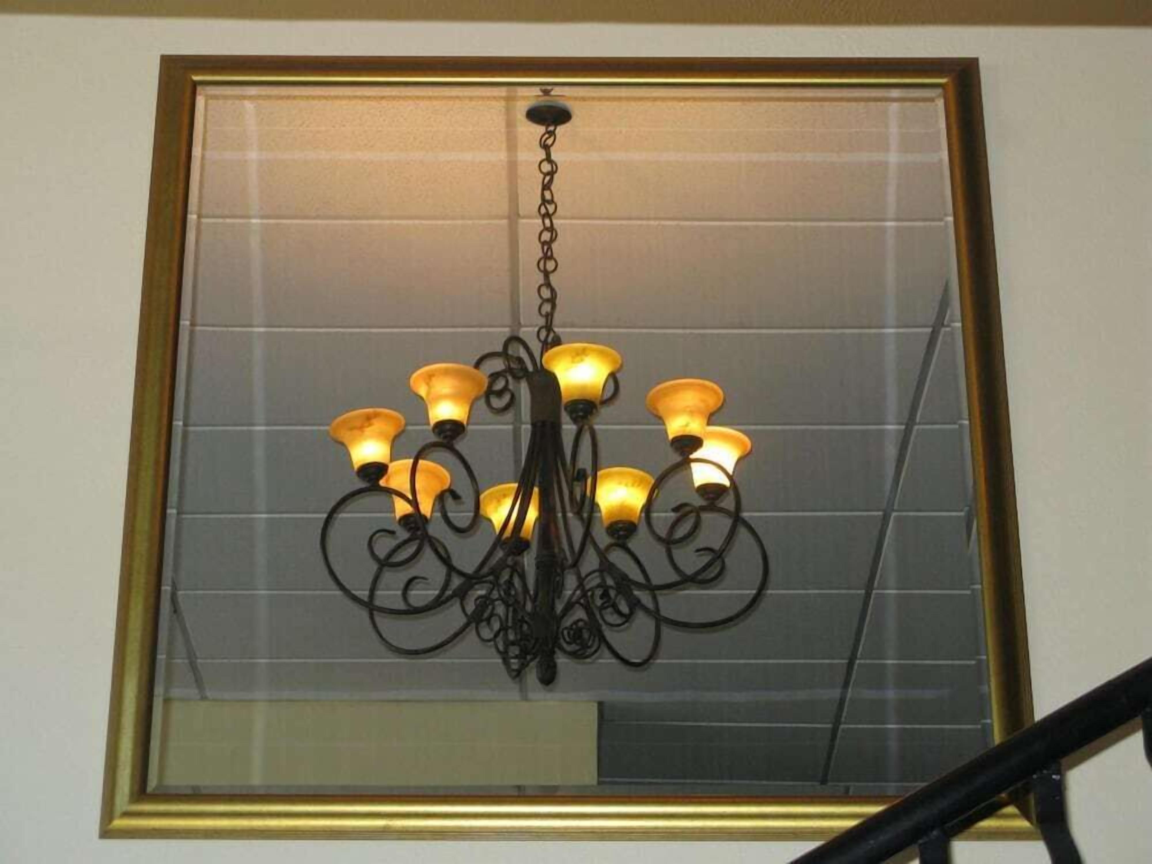 Ein Kronleuchter mit mehreren Lichtern, der an einer Kette von einer Wand hängt, unter der sich ein großer Spiegel befindet.