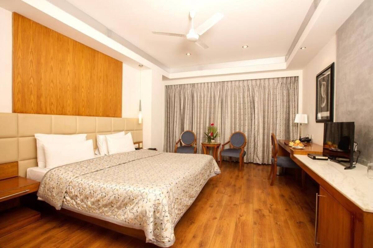 A hotel room with a bed, a desk, a chair, a television, and a ceiling fan.