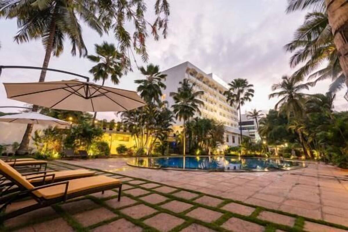 A hotel with a pool, palm trees, and lounge chairs.