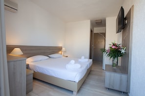 A hotel room with a bed, bedside tables, a TV, and a flower arrangement. - Apollon (Agios Nikolaos)