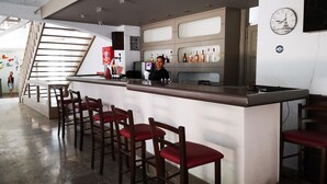 A bar area with a counter, multiple stools, and a staircase in the background. - Apollon (Agios Nikolaos)