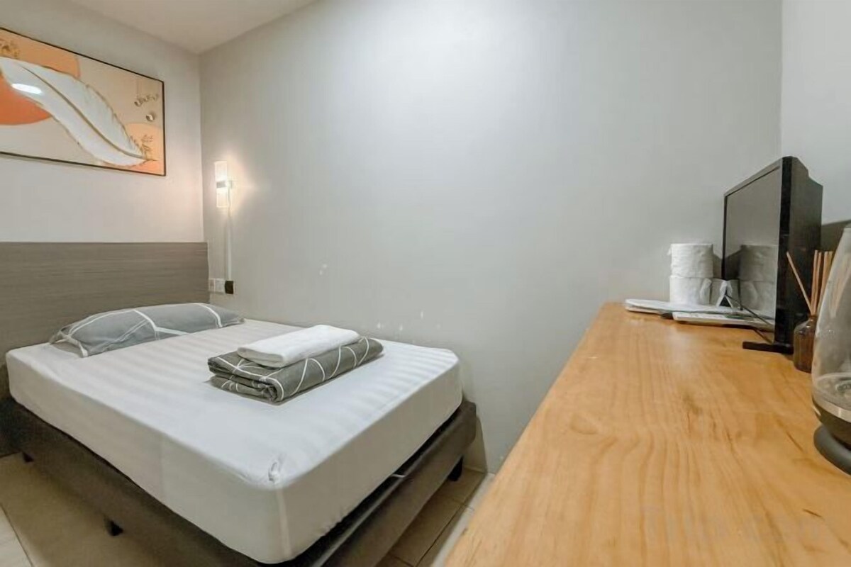 A hotel room with a bed, bedside table, lamp, and a painting on the wall.