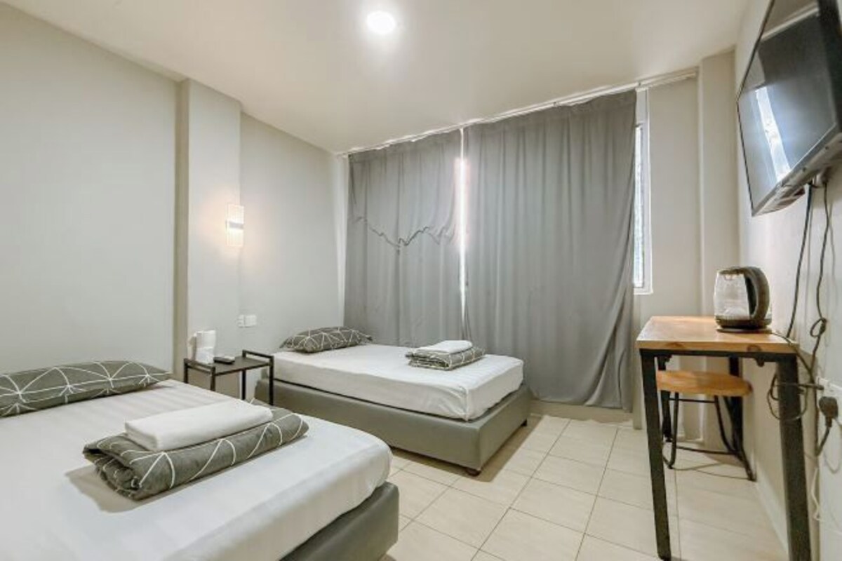 A hotel room with two beds, a desk, a television, and a window with curtains.