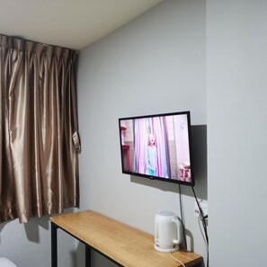 A room with a television mounted on the wall, a wooden table, and a kettle on the table. - Haising (SINGAPORE)