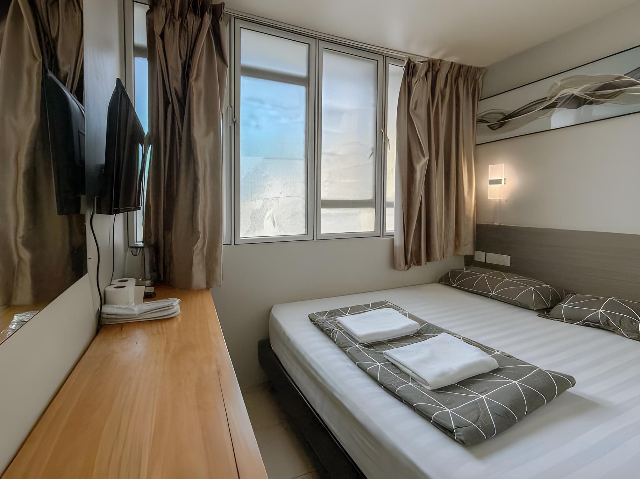 A hotel room with a bed, a desk with a telephone, a television, and a window with curtains.