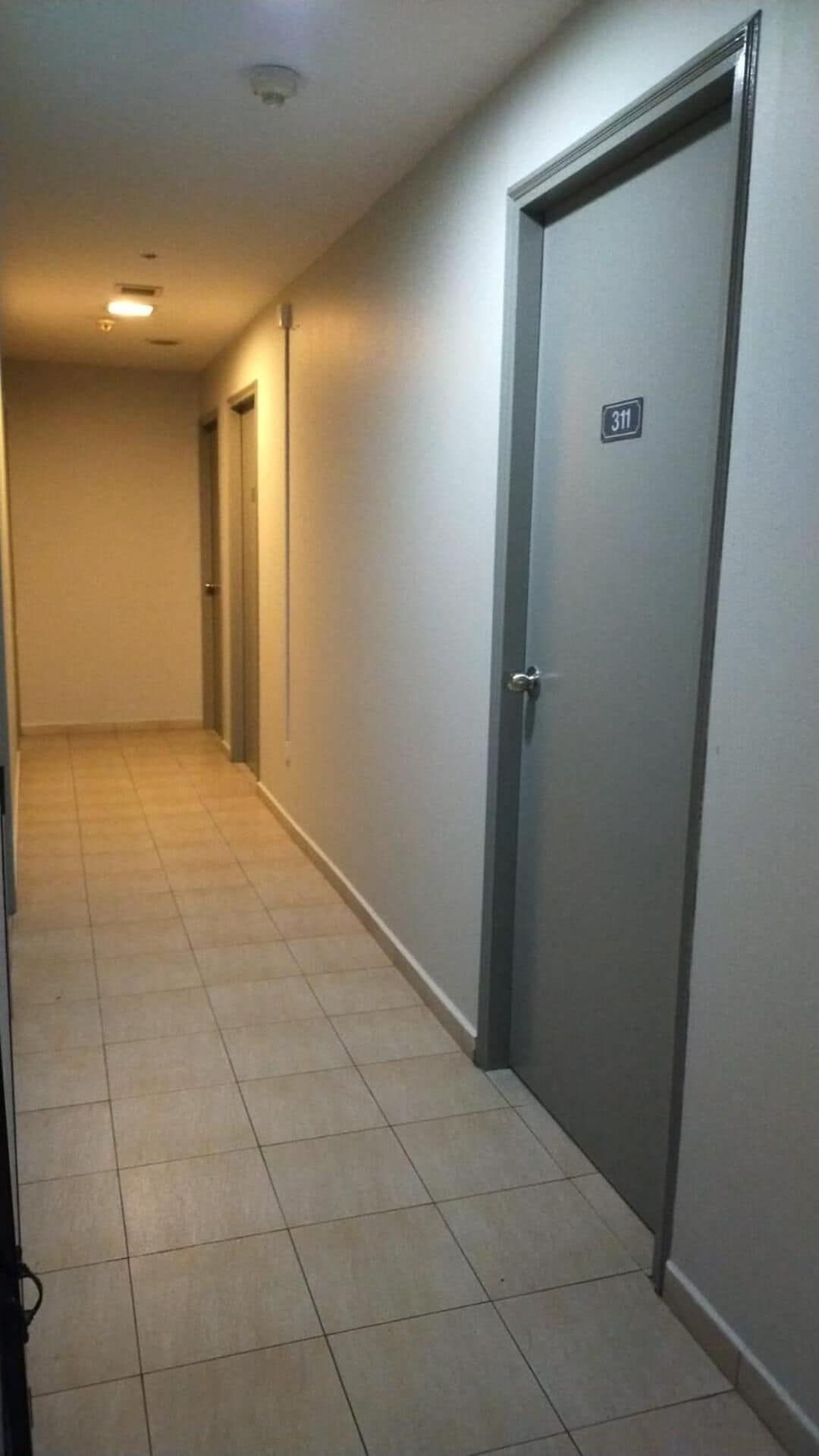 Un pasillo con suelo de baldosas, una puerta marcada con el número 311 y otra puerta con manija.
