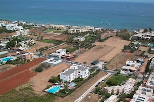 Vista aérea de una zona residencial costera con edificios, campos abiertos y una playa.