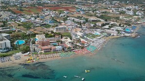 An aerial view of a coastal town with a beach, buildings, and boats. - Altis Hotel (Malia)