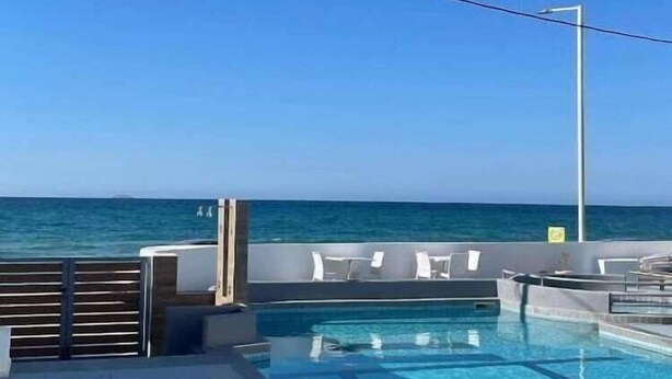 Zona de piscina con vista al océano, un espacio de descanso con sillones blancos y un cielo azul despejado.