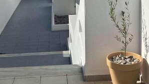 Una terraza moderna al aire libre con una planta en maceta, paredes blancas y una vista despejada del cielo.