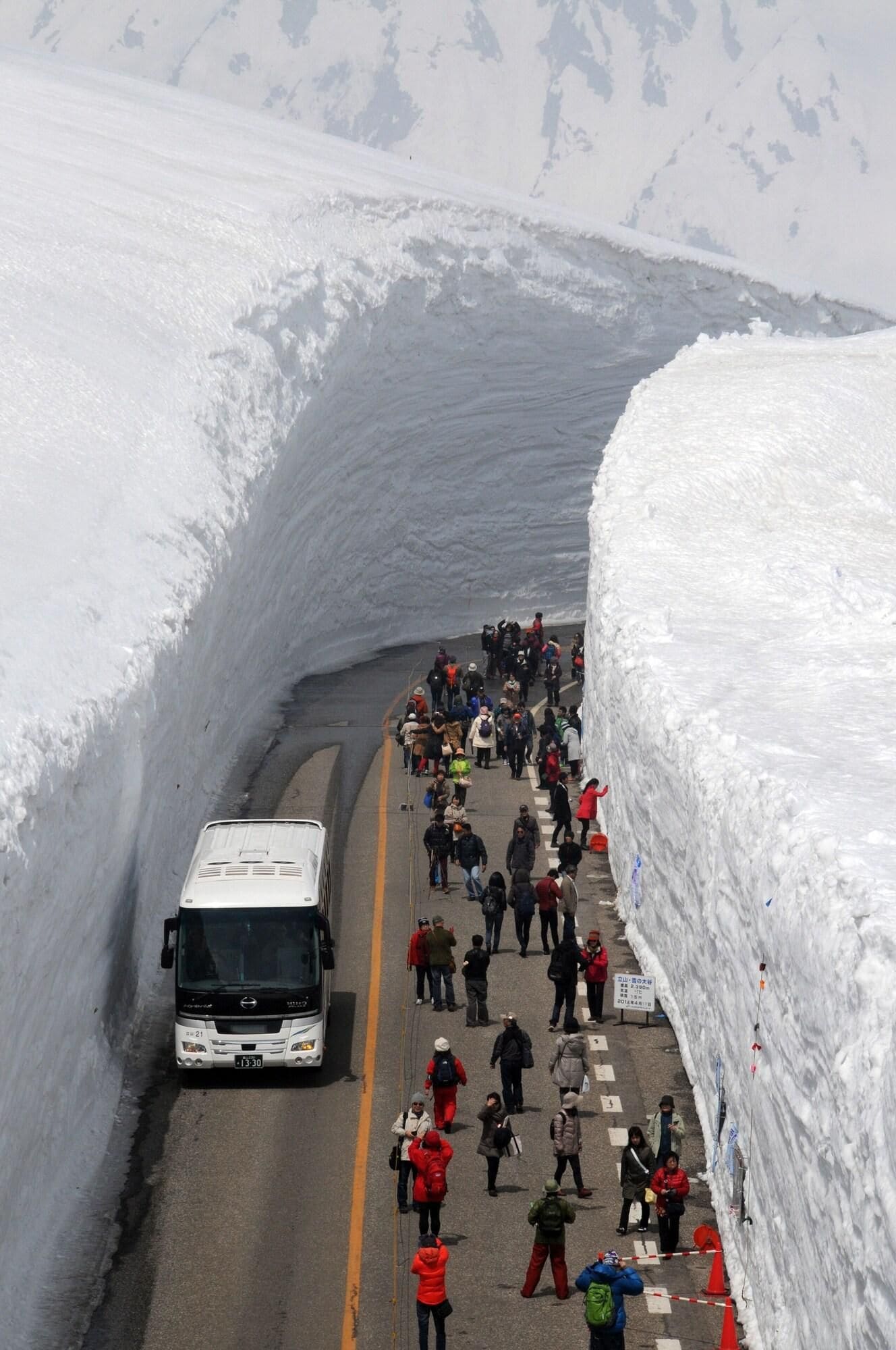 A snow-covered road with a bus and pedestrians.