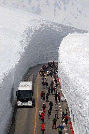 A snow-covered road with a bus and pedestrians. - Midagahara Hotel (Tateyama)