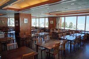Un comedor amplio con varias mesas y sillas, y ventanas grandes que ofrecen vistas a montañas nevadas.