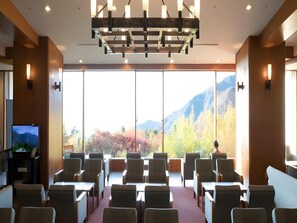 A conference room with a large window offering a mountain view, a television on the left, and a modern chandelier. - Midagahara Hotel (Tateyama)