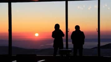 Twee silhouetten voor een zonsondergang, staand voor een groot raam met uitzicht op het landschap.