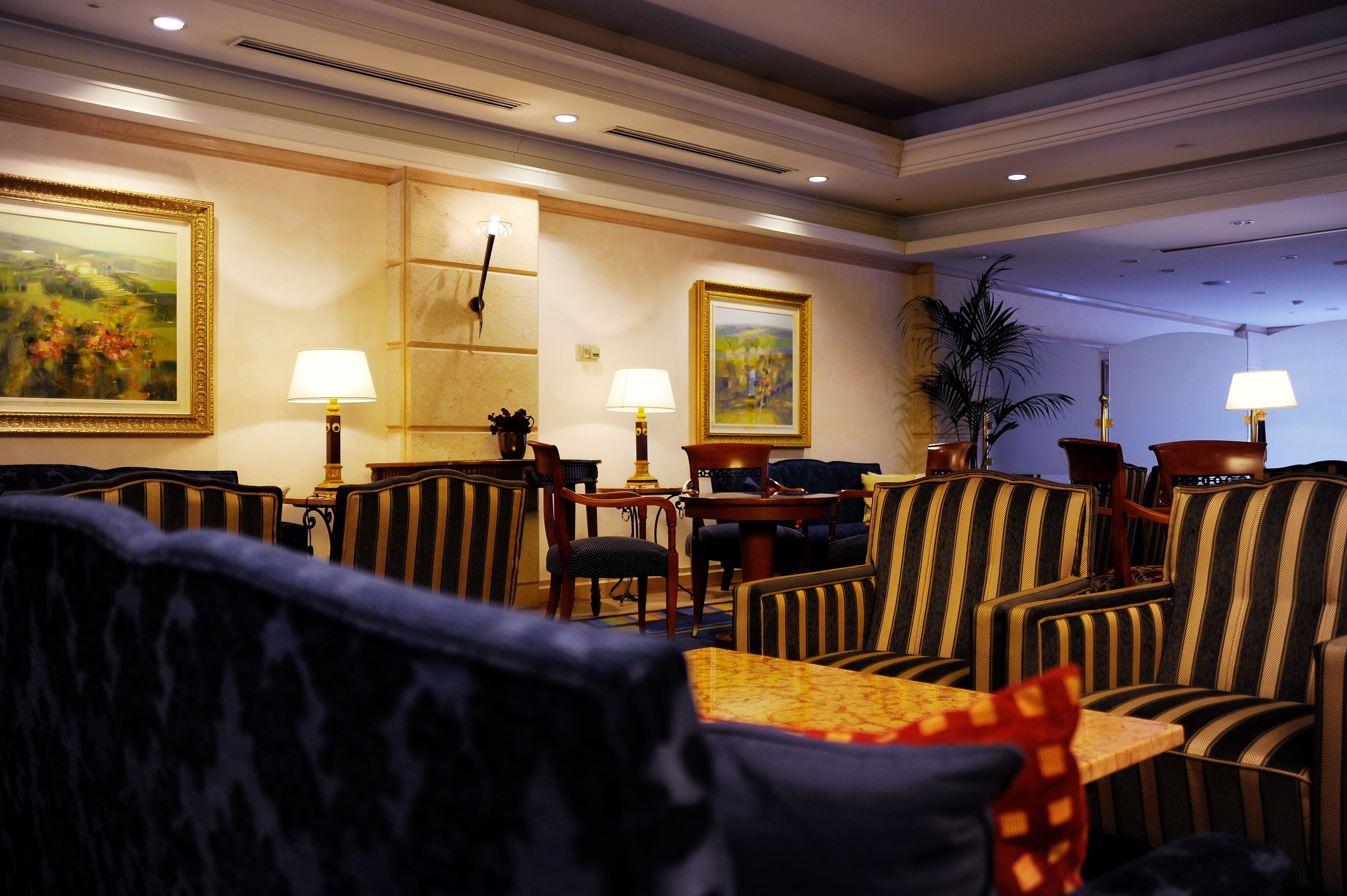 A hotel lobby with striped upholstered chairs, a wooden coffee table, and two paintings on the walls.