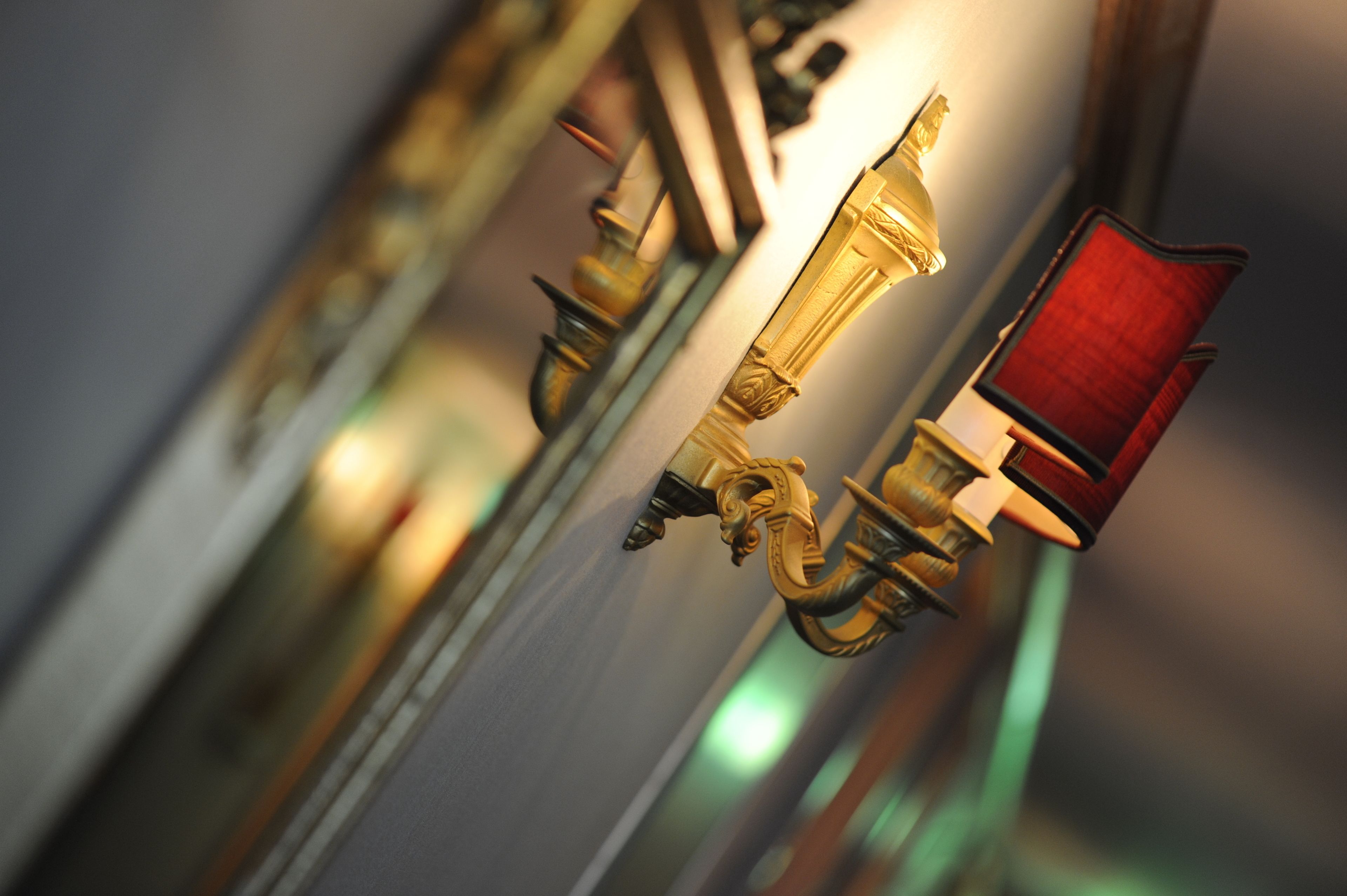 A close-up of a brass door handle with a red panel, reflecting in a mirror.