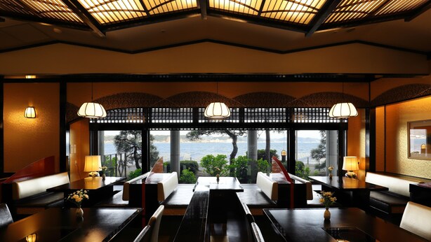 A restaurant with a view of the sea, featuring dark wooden tables and chairs, and decorative lamps. - Kamakura Park Hotel (Kamakura)