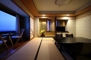 A traditional Japanese-style room with tatami flooring, a low table, and chairs. There is a television on a stand, a small table with a bowl, and a vase with flowers. - Kamakura Park Hotel (Kamakura)