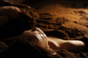 Una persona recostada sobre una superficie texturizada, que podría ser una cama o un sofá, en un ambiente con poca luz.