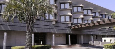 Un hotel moderno con fachada simétrica, amplias ventanas y una palmera en primer plano.