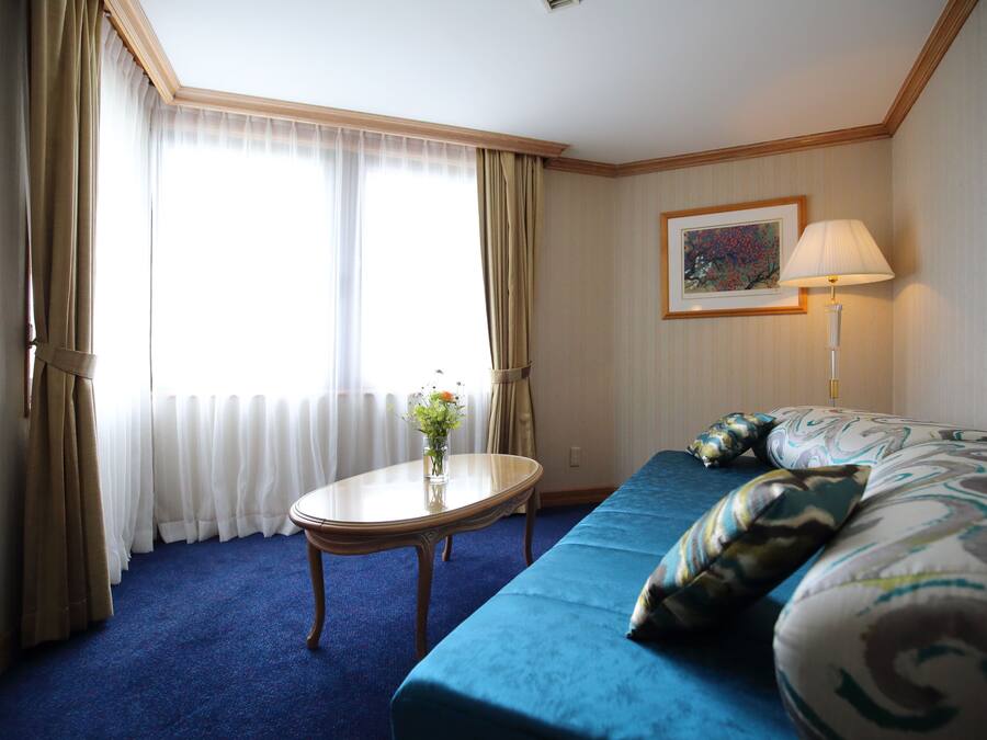 A hotel room with a large bed, a small table with a vase of flowers, and a lamp.