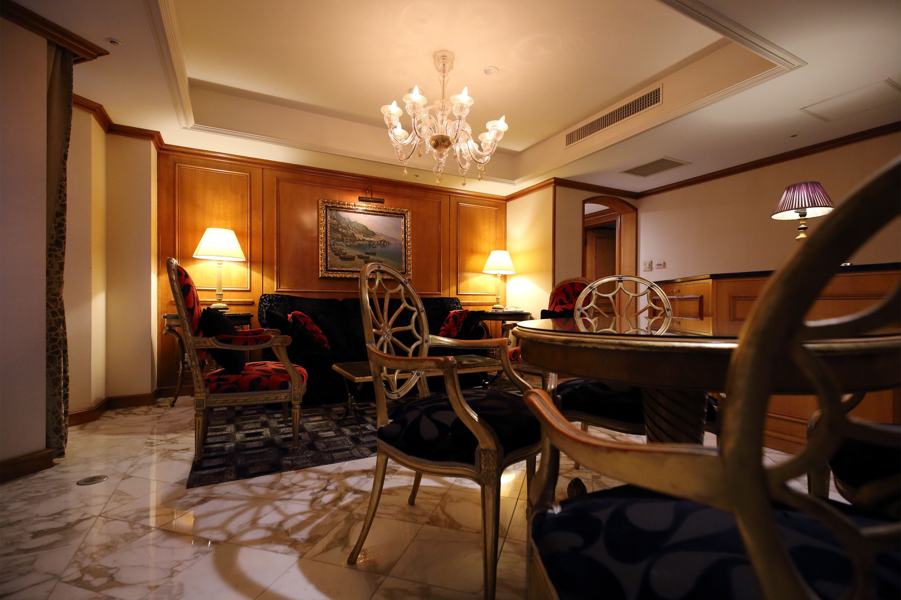 A dining area with wooden paneling, a chandelier, and two lamps.