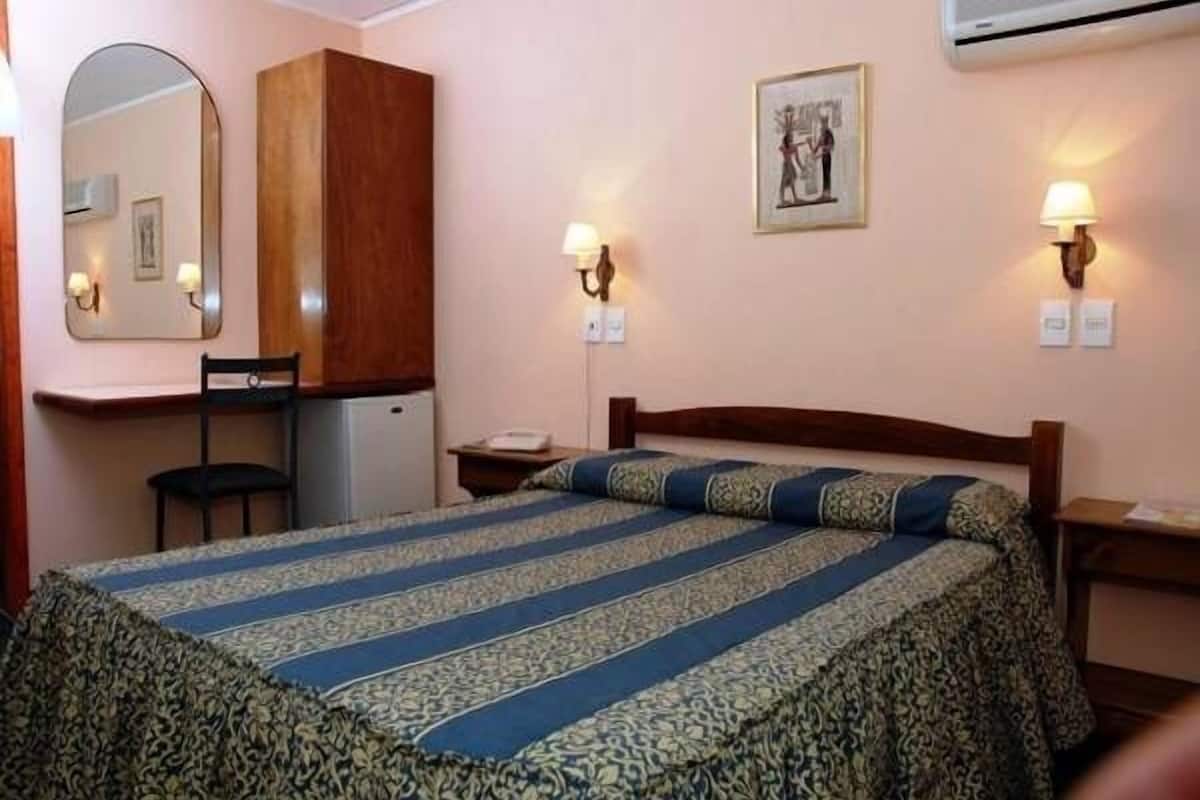 A hotel room with a bed, a desk, a chair, a wardrobe, and two wall-mounted lamps.