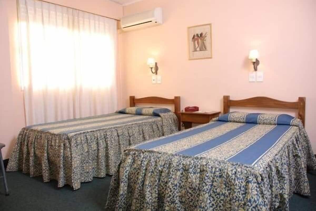 A hotel room with two beds, a nightstand, a lamp, and an air conditioner.