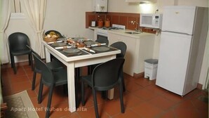 Eine kompakte Küche mit Esstisch für vier Personen, inklusive Kühlschrank, Mikrowelle und Gasherd.