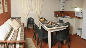 Ein kompakter Wohnraum mit Esstisch für vier Personen, einer Couch, einer Küchenzeile und einem Fenster mit Vorhängen.