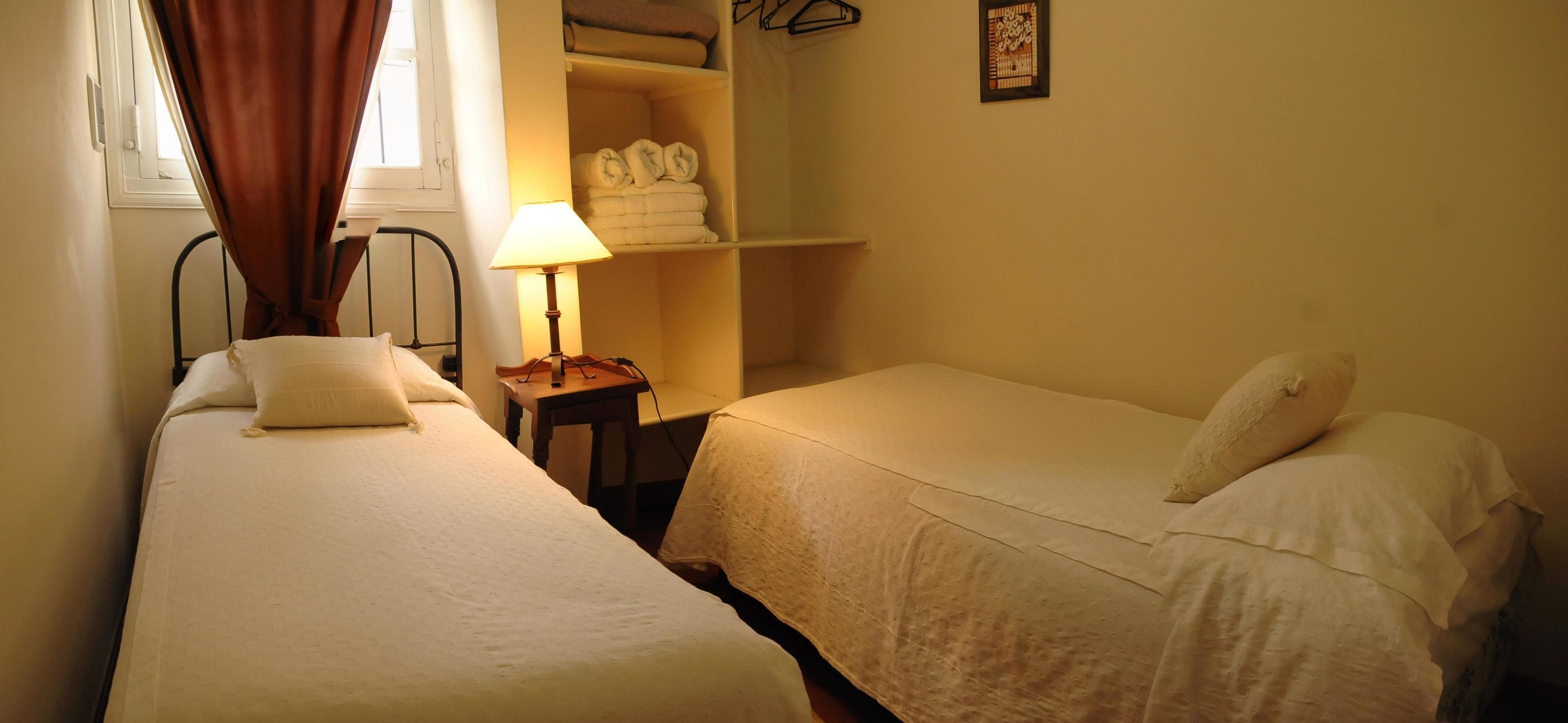A small, cozy bedroom with two single beds, a bedside table with a lamp, and a wardrobe with folded towels.