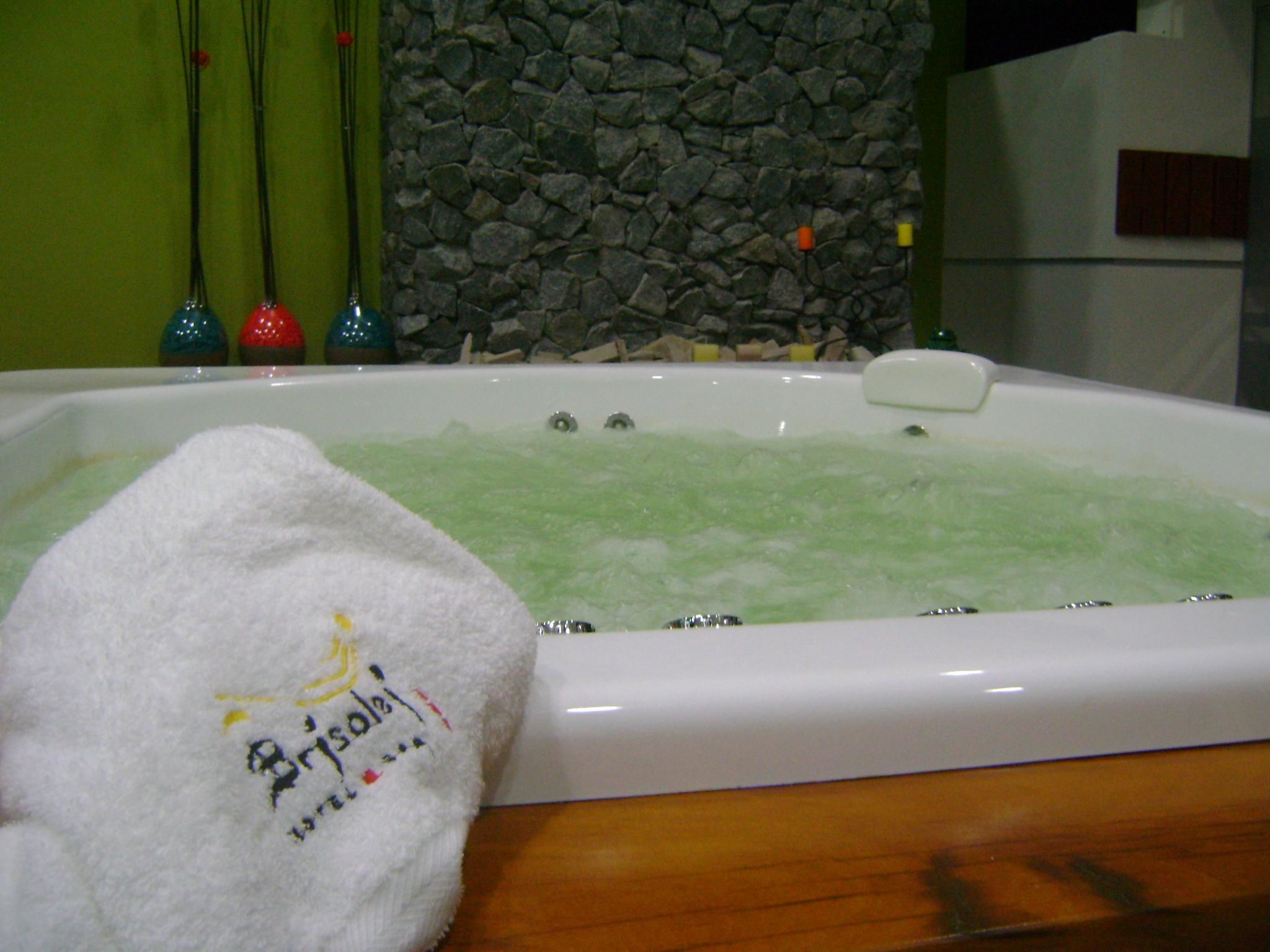 Una bañera con una toalla blanca al lado, una pared de piedra y un suelo de madera.