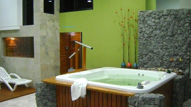 Un espace de bien-être comprenant un jacuzzi, des murs en pierre et un banc en bois.